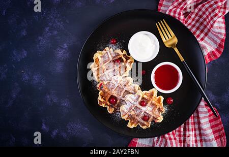 Waffle belgi tradizionali con frutti di bosco, panna acida e marmellata sul tavolo scuro. Vista dall'alto, dall'alto Foto Stock