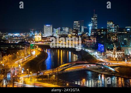 Vilnius, capitale della Lituania, panorama notturno panoramico aereo degli edifici moderni del distretto finanziario con il fiume Neris e il ponte Foto Stock