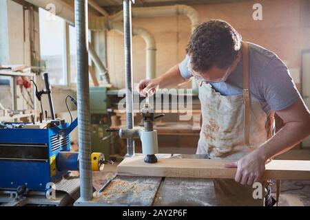 Falegname come produttore di mobili lavora con asse di legno su un trapano Foto Stock