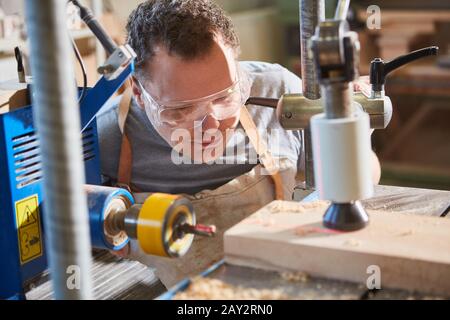 Falegname con occhiali di sicurezza durante la foratura del legno con un trapano laser Foto Stock