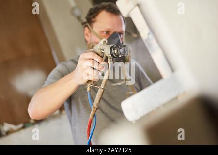 Pittore con protezione respiratoria e pistola a spruzzo macchia o vernice il legno Foto Stock