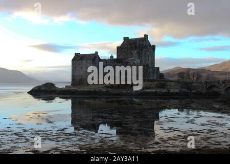 Lo splendido Castello di Eilan Donan si riflette perfettamente nelle acque scozzesi in una giornata ancora irta con il sole che colpisce le colline Foto Stock