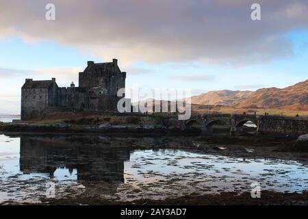 Lo splendido Castello di Eilan Donan si riflette perfettamente nelle acque scozzesi in una giornata ancora irta con il sole che colpisce le colline Foto Stock