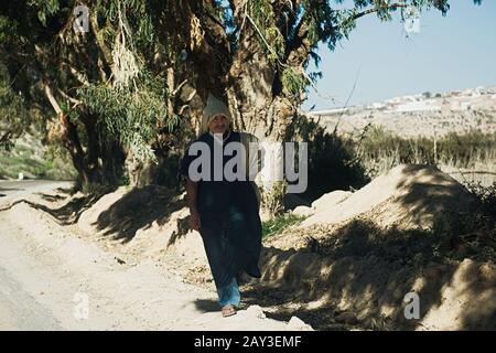 Essaouira, MAROCCO - 17 GENNAIO 2020: Un uomo musulmano cammina lungo la strada all'ombra degli alberi. Foto Stock