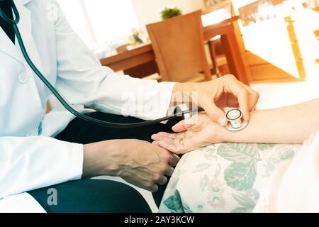 closeup di un medico caucasico, in una mano bianca, che prende l'impulso ad una donna di pazienti caucasici anziani con uno stetoscopio, a casa sua o a un nursi Foto Stock