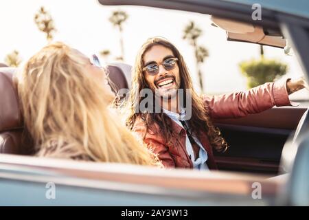 Felice giovane coppia fare viaggio su strada in città tropicale - Viaggiare persone che si divertono a guidare in auto convertibile alla scoperta di nuovi luoghi Foto Stock