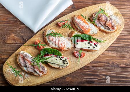 Panini con pesce rosso, manzo in suvit e formaggio morbido. Guarnita con fette di verde, rucola e pomodori. Su un vassoio ovale in legno. Copiare lo spazio Foto Stock