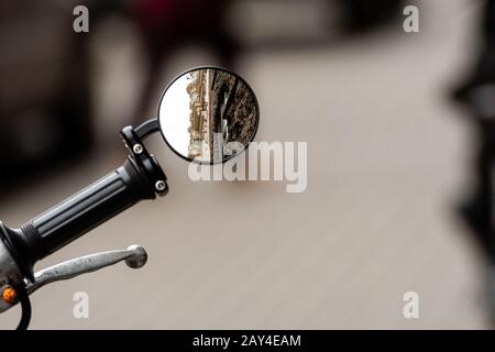 riflesso di un antico edificio residenziale nello specchio retrovisore di una motocicletta di fronte ad un defocused marciapiede Foto Stock