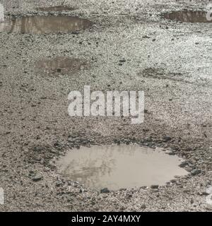 Luce riflessa da pozzanghere d'acqua su pista di campagna. Per le cadute di poole, le pozzanghere dell'acqua, il riflesso dell'acqua, la superficie irregolare, la superficie irregolare, lo stato scadente. Foto Stock