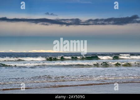 LOSSIEMOUTH MORAY FIRTH SCOTLAND UN INVERNO WEST BEACH E LE ONDE E ATTRAVERSO IL FIRTH LE COLLINE INNEVATE DI SUTHERLAND Foto Stock