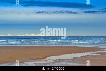 LOSSIEMOUTH MORAY FIRTH SCOTLAND WINTER BEACH E LE ONDE CON LE COLLINE INNEVATE DI SUTHERLAND Foto Stock