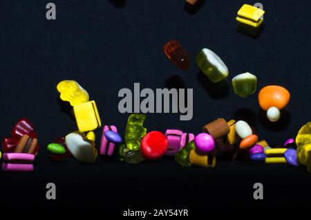 Molti dolci e colorati caramelle stanno cadendo giù ad un tavolo nero Foto Stock