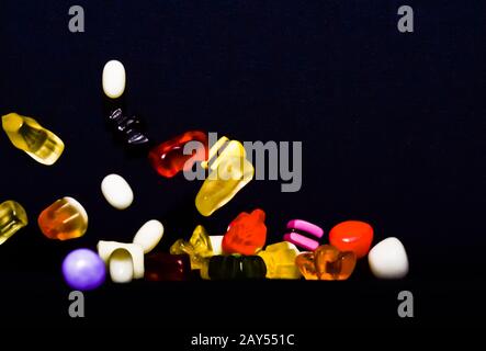 Molti dolci e colorati caramelle stanno cadendo giù ad un tavolo nero Foto Stock