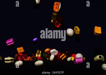 Molti dolci e colorati caramelle stanno cadendo giù ad un tavolo nero Foto Stock
