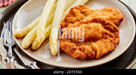 Spighe di asparagi bianchi di stagione con pesce fritto croccante o schnitzel in una vista ravvicinata su un piatto per la pubblicità del menu Foto Stock