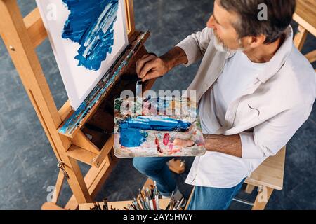 Vista ad alto angolo della tavolozza di contenimento per artista maschile e coltello per pittura Foto Stock