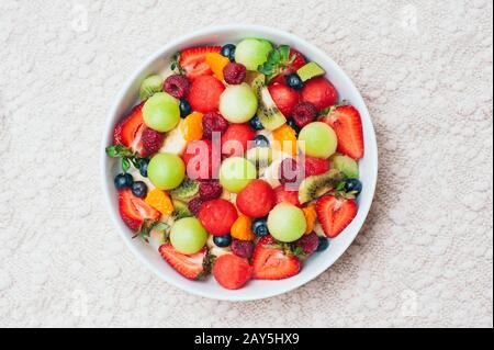 Insalata di frutta fresca e sana in ciotola. Fette di fragola, lampone, kiwi, mandarino, mirtillo su piastra. Frutti deliziosi. Piatto vegetale. corr. Matura Foto Stock