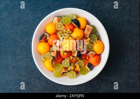 Piatto di frutta sano. Messa a fuoco selettiva. Ciotola di mango colorato tagliato, fichi, uva e papaia su sfondo scuro. Delizioso piatto vegetariano. Foto Stock