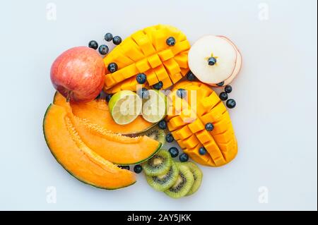 Assortimento di succosa frutta tropiale su sfondo bianco. Fette di melone, mango arancione, kiwi, lime, mirtilli e mela. Piatto vegetale. Foto Stock