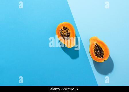 Frutta di papaia matura tagliata a metà su fondo blu duotone, in luce dura. Sopra la vista delle metà di frutta di papaia. Dolce frutta tropicale. Primo piano di papaia. Foto Stock