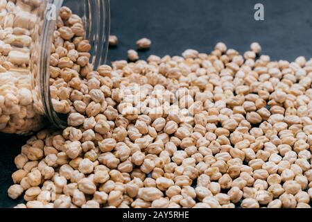 Vaso in vetro con garbanzo grezzo. Granelli di ceci isolati su sfondo scuro. Primo piano. Semi proteici. Cibo sano. Ingrediente vegano Foto Stock