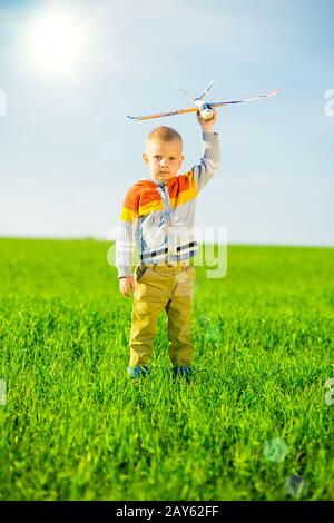 Felice ragazzo giocando con aeroplano giocattolo contro il Cielo di estate blu e verde dello sfondo dei campi. Foto Stock