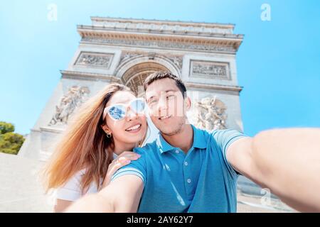 Un uomo felice e una ragazza abbracciano e fotografano un selfie contro l'Arco di Trionfo a Parigi. Luna di miele e un viaggio insieme in Francia Foto Stock