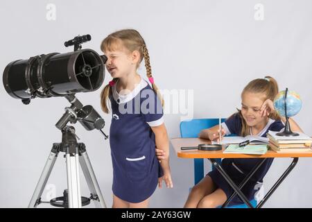 Astronomo ragazza guarda attraverso l'oculare del telescopio, e l'altra ragazza seduta felicemente al tavolo Foto Stock