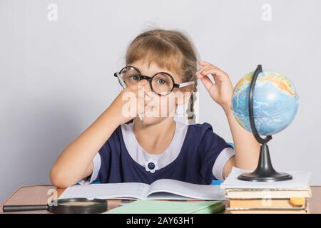 Schoolgirl corregge bicchieri seduti ad una scrivania in aula geografia Foto Stock