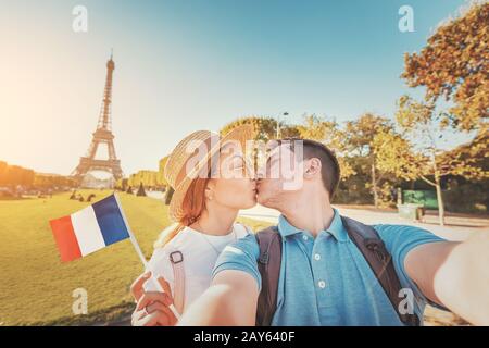 Coppia mista di gara in amore abbracciando e prendendo selfie con la bandiera francese e la Torre Eiffel sullo sfondo. Viaggio di nozze in Francia e Parigi Concept Foto Stock