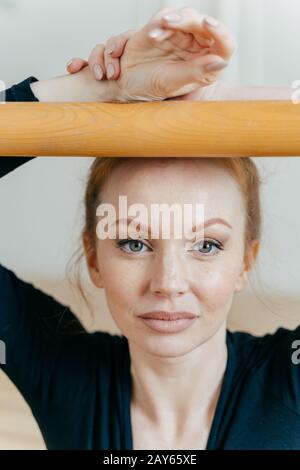 Testa di talento ballerina femminile abili pose vicino barre, ha occhi blu, pelle sana, aspetto accattivante, pratica danza nella sala da ballo Foto Stock