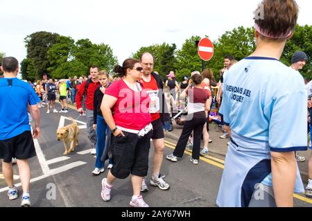 Gruppi di persone e corridori che si raccolgono sulla strada prima dell'inizio di UNA corsa di beneficenza 10KM. Donna sovrappeso in primo piano con runner. Foto Stock