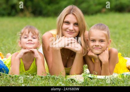 La madre e le sue due figlie si trovano sull'erba verde e appoggiando le mani una testa guardato nella foto Foto Stock