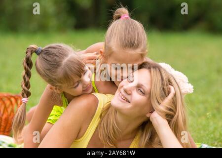 Due figlia baciando e abbracciando la madre sdraiati sull'erba su un picnic Foto Stock