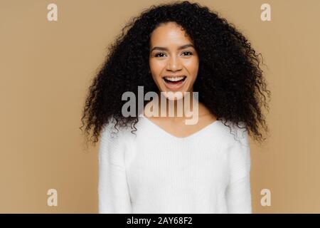 Headshot di sano positivo modello femminile ride felicemente, ha bush capelli afro, vestito in bianco morbido ponticello, felice di ricevere il complimento dal ragazzo Foto Stock