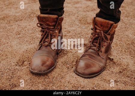 Immagine di uomo irriconoscibile si erge su terreno sabbioso in pelle marrone vecchie scarpe shaggy con lacci. Scarpe uomo. Scatto all'aperto Foto Stock