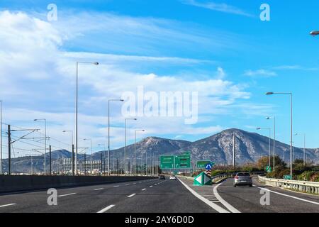 Esci sull'autostrada in Grecia lasciando Atene verso la penisola del Peloponneso con le montagne sullo sfondo e le indicazioni in greco e inglese Foto Stock