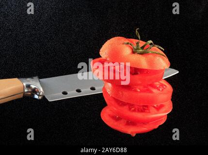 Pomodoro a fette rosso con lama di coltello sullo sfondo di polvere d'acqua nella retroilluminazione di uno sfondo nero. Spazio di copia, immagine orizzontale. Foto Stock