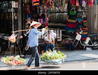 Donna vietnamita che porta cesti di frutta e verdura per strada a Hue, Vietnam Foto Stock