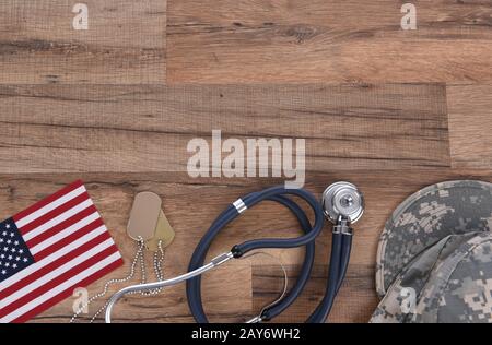 Concetto Di Assistenza Sanitaria Militare. Camo cappello, tag cane, stetoscopio, pillole, e American Flags su uno sfondo di legno. Foto Stock