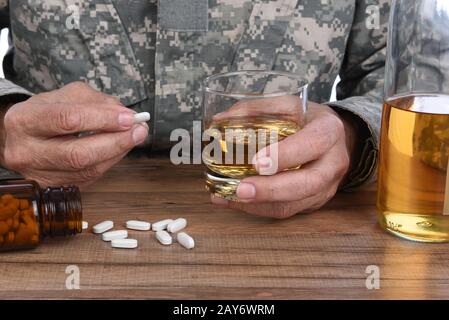 Concetto militare di abuso di droghe e alcool. Primo piano di soldato con whisky e pillole per trattare i suoi sintomi PTSD. Foto Stock