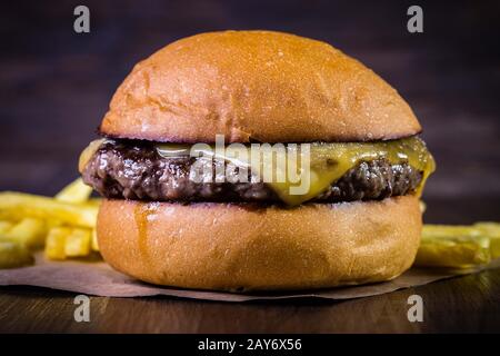 Hamburger di manzo artigianale con formaggio e patatine fritte su tavola di legno e sfondo rustico Foto Stock