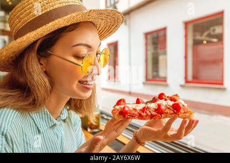 Divertente ragazza asiatica in cappello mangiare focaccia sorta di pizza Foto Stock