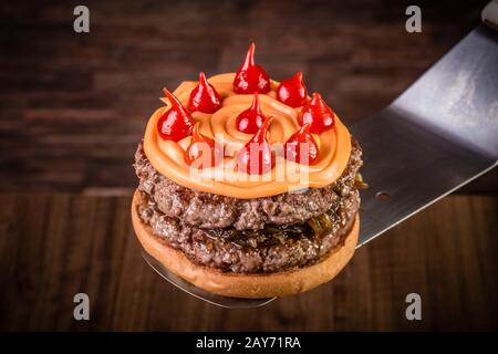 Hamburger doppio di manzo artigianale con formaggio cheddar, cipolla caramellata e pepe pout su tavola di legno e sfondo rustico Foto Stock