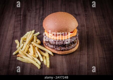 Hamburger doppio di manzo artigianale con formaggio cheddar, cipolla caramellata e pepe pout su tavola di legno e sfondo rustico Foto Stock