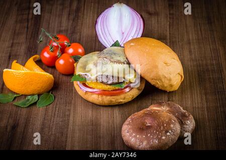 Hamburger vegetariano artigianale con formaggio, arancia, foglie di basilico, funghi shiitake e cipolla viola su tavola di legno e sfondo rustico Foto Stock