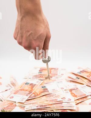 Una mano dell'uomo tiene una chiave sopra un mucchio di cinquemila-ruble fatture.Il concetto di migliorare le condizioni dell'alloggiamento. Foto Stock