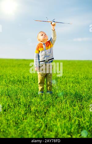 Felice ragazzo giocando con aeroplano giocattolo contro il Cielo di estate blu e verde dello sfondo dei campi. Foto Stock