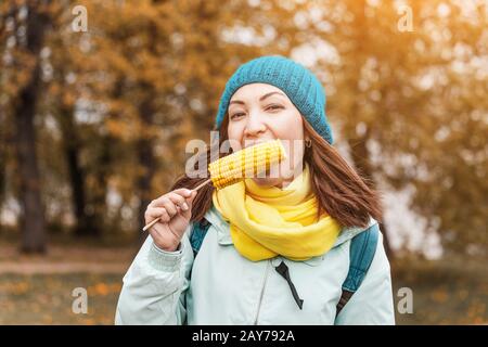 giovane donna che mangia mais bollito nel parco in autunno Foto Stock