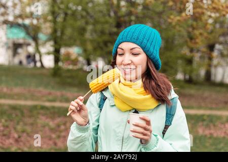 giovane donna che mangia mais bollito nel parco in autunno Foto Stock